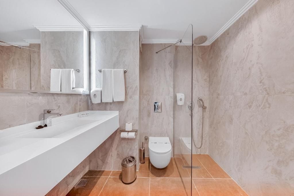 Uma casa de banho moderna com uma grande pia branca, sanita e área de duche.