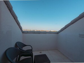 A small balcony with a view of a distant cityscape, a chair, and a small table.