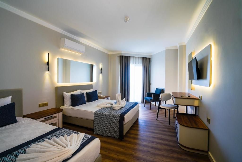 Habitación de hotel con dos camas, un escritorio, una silla, un televisor y un ventanal con cortinas.