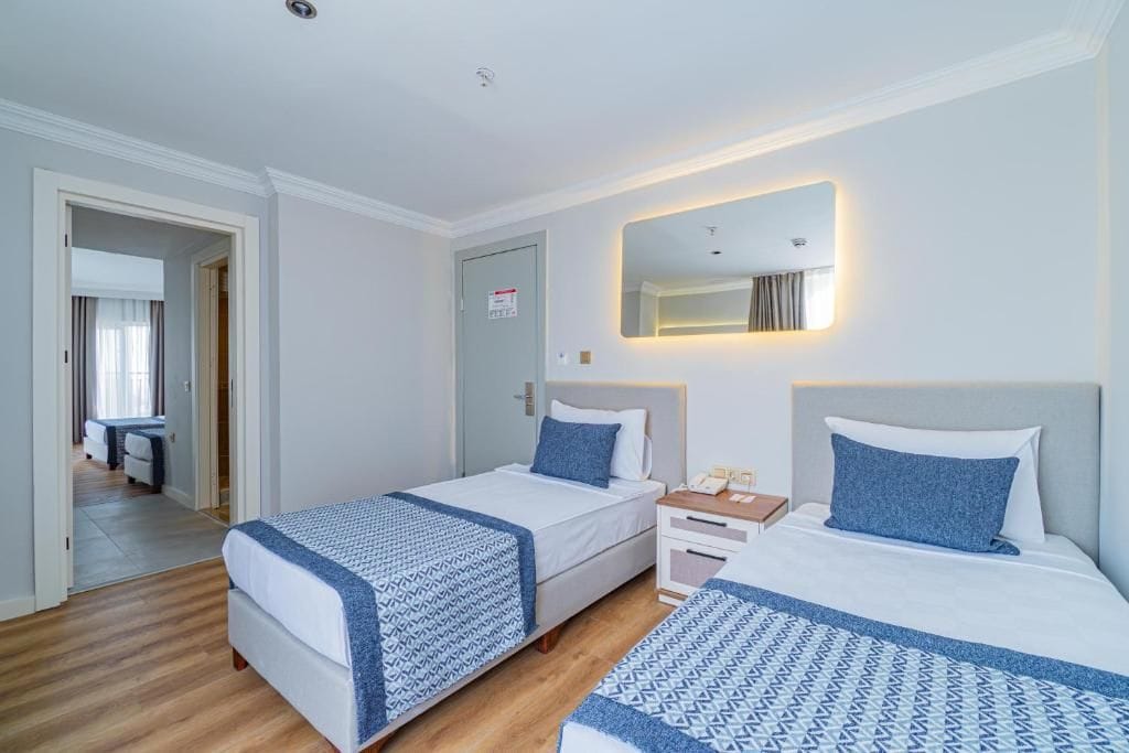 A hotel room with two beds, a bedside table with a phone, a mirror, and a door.