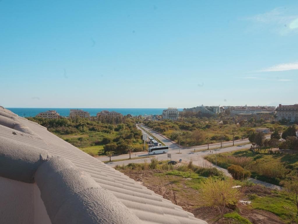 A coastal cityscape with a road leading to a beach, buildings in the distance, and a clear sky.