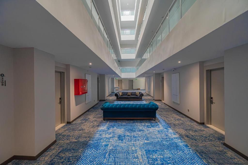 A hotel corridor with a patterned carpet, a blue sofa, and a skylight ceiling.