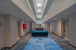 A hotel corridor with a patterned carpet, a blue sofa, and a skylight ceiling.