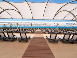 A beachside seating area with rows of lounge chairs and a wooden walkway leading to the water.
