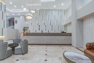 Uma área de recepção moderna, com piso de mármore, balcão de atendimento e espaço de espera com sofás e cadeiras.