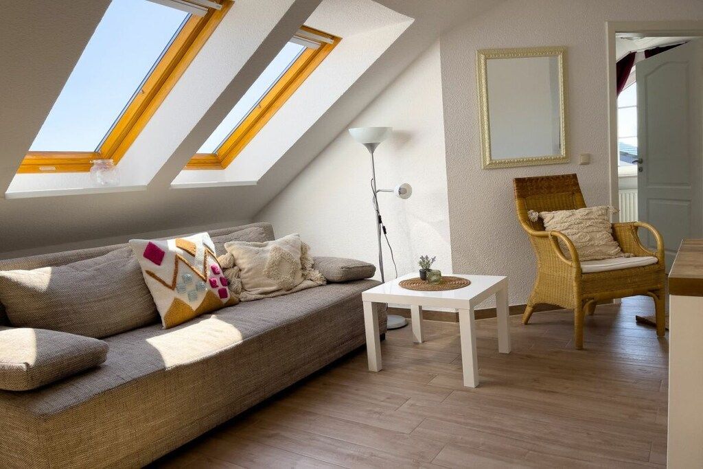 A room with a sloped ceiling, a sofa, a chair, a small table, and a floor lamp.