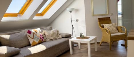 A room with a sloped ceiling, a sofa, a chair, a small table, and a floor lamp.