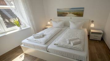 A double bed with white linens, two bedside tables with lamps, a window with curtains, and a painting on the wall.