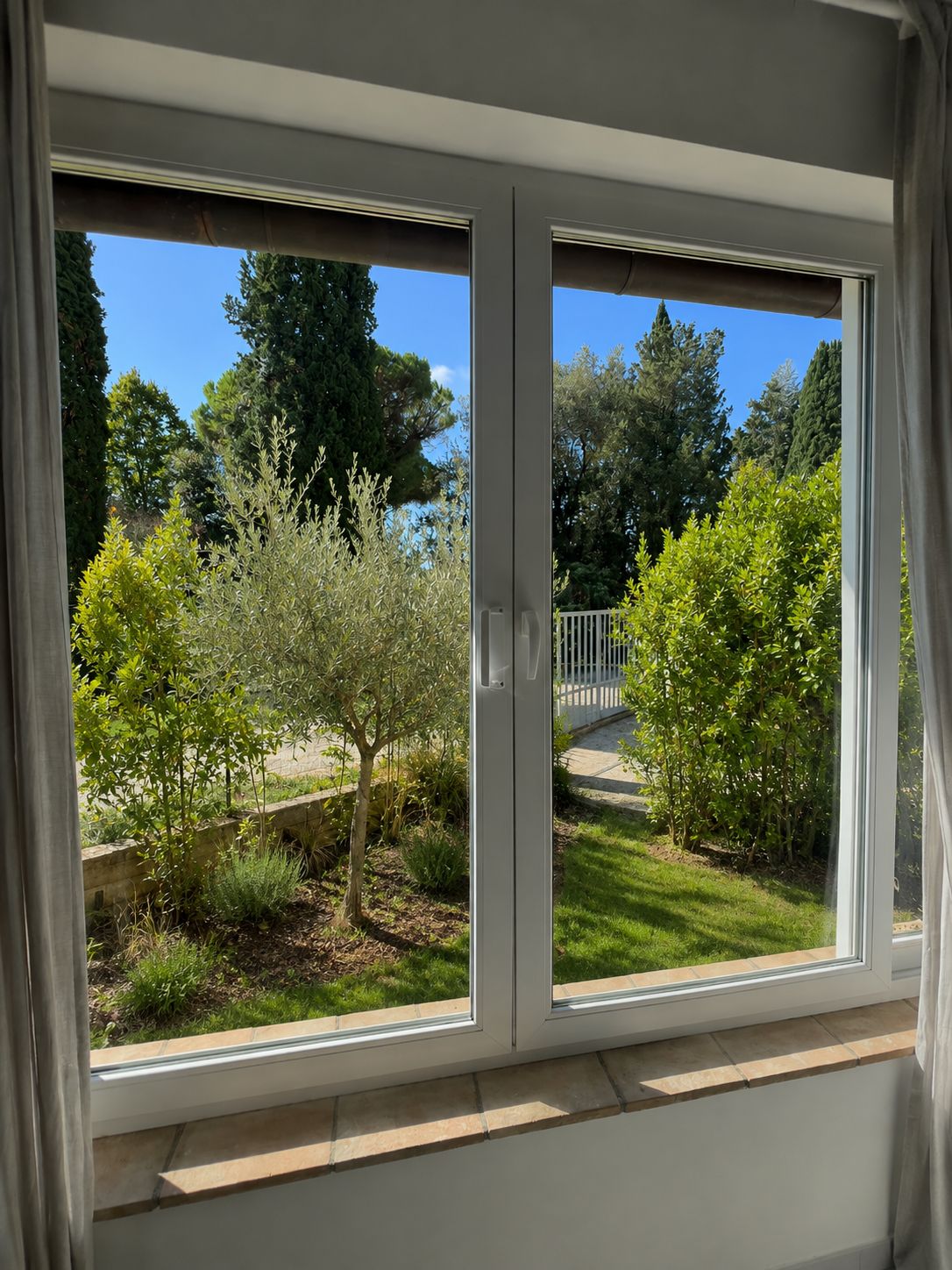 Una finestra con vista su un giardino, tra cui alberi e un recinto bianco.