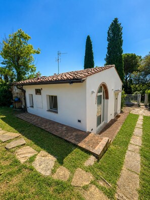 A small, single-story building with a tiled roof, a stone pathway leading to the entrance, and a well-maintained lawn.