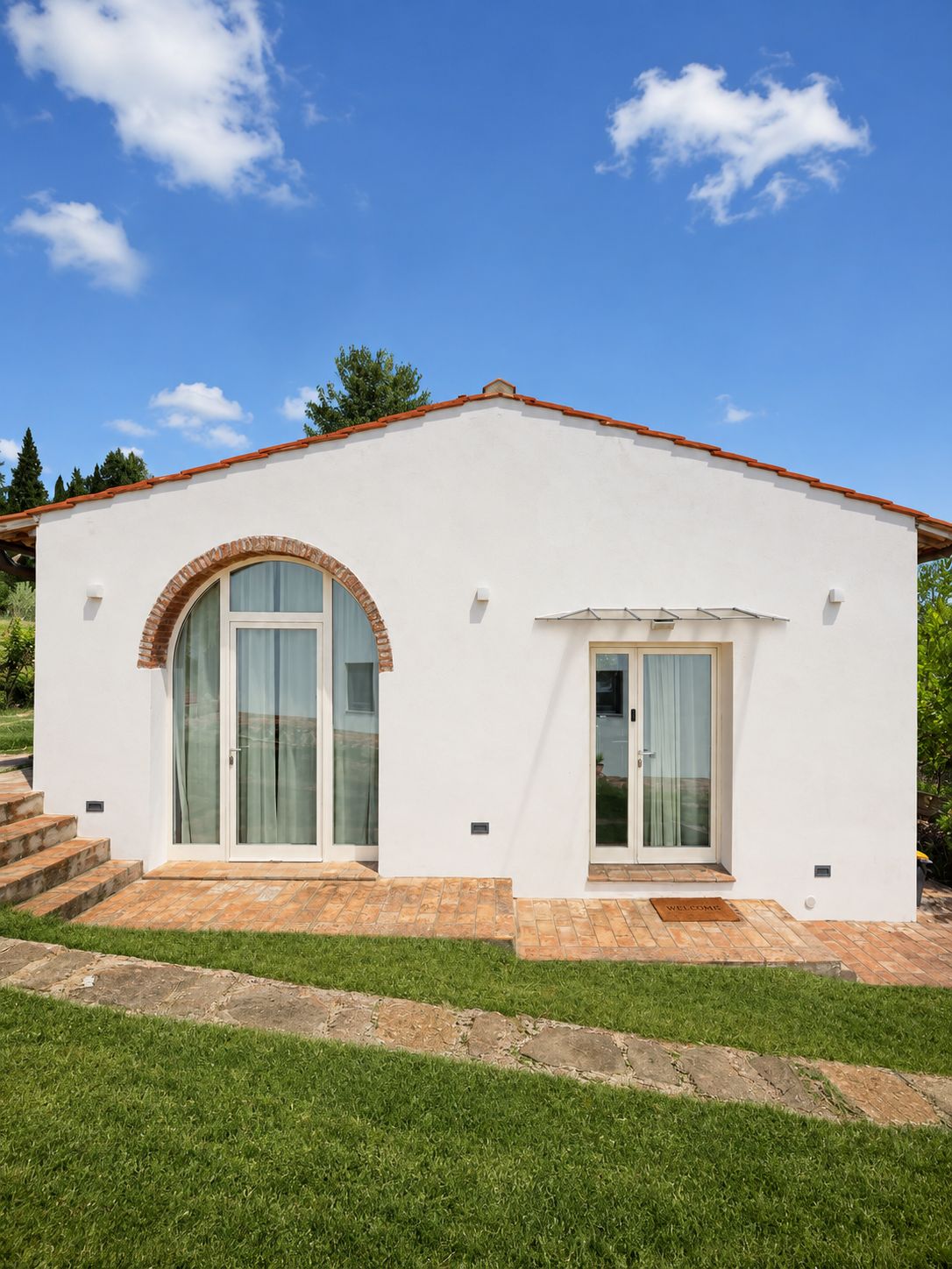 Un bâtiment d’un seul étage, à l’extérieur blanc, avec un toit recouvert de tuiles rouges et une entrée en forme d’arc en briques.