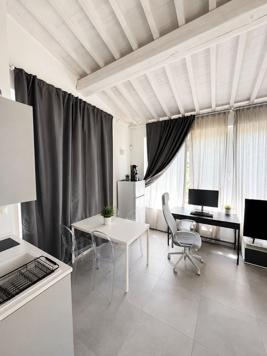 A modern office space with a white desk, clear plastic chairs, a computer, and a coffee machine.