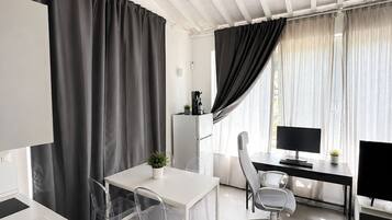 A modern office space with a white desk, clear plastic chairs, a computer, and a coffee machine.