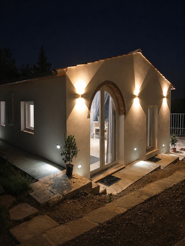 A modern house with a large arched doorway, exterior lighting, and a potted plant.