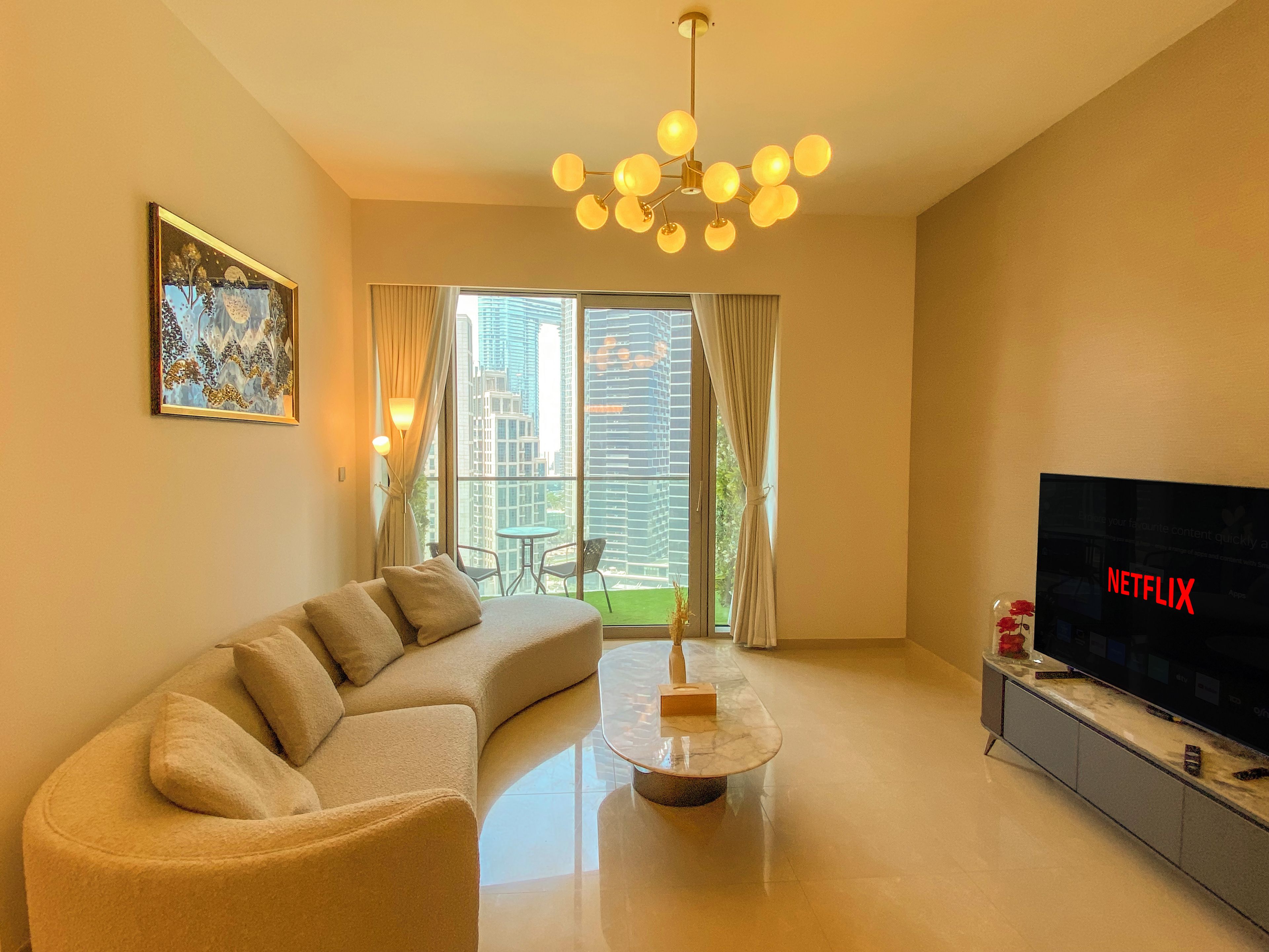 A modern living room with a sectional sofa, a coffee table, a television, and a large window with curtains.