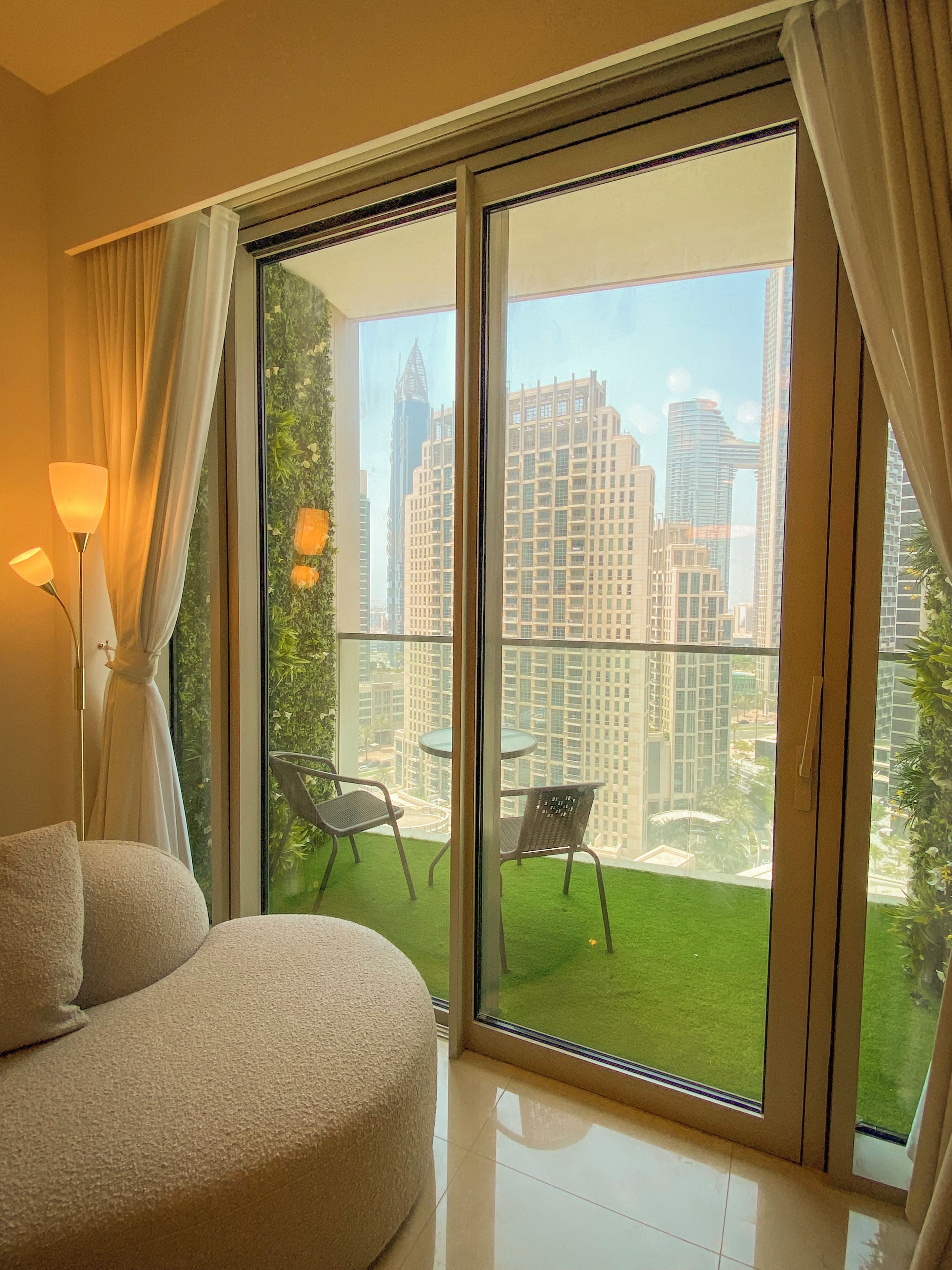 A modern hotel room with a large sliding glass door leading to a balcony with a view of city buildings.