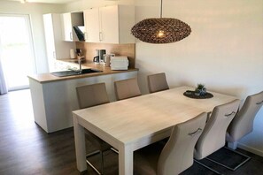 A modern kitchen with a dining area, featuring a light wood table, beige chairs, and a woven pendant light. - House No. 20, Fischerhus (Wangerland)