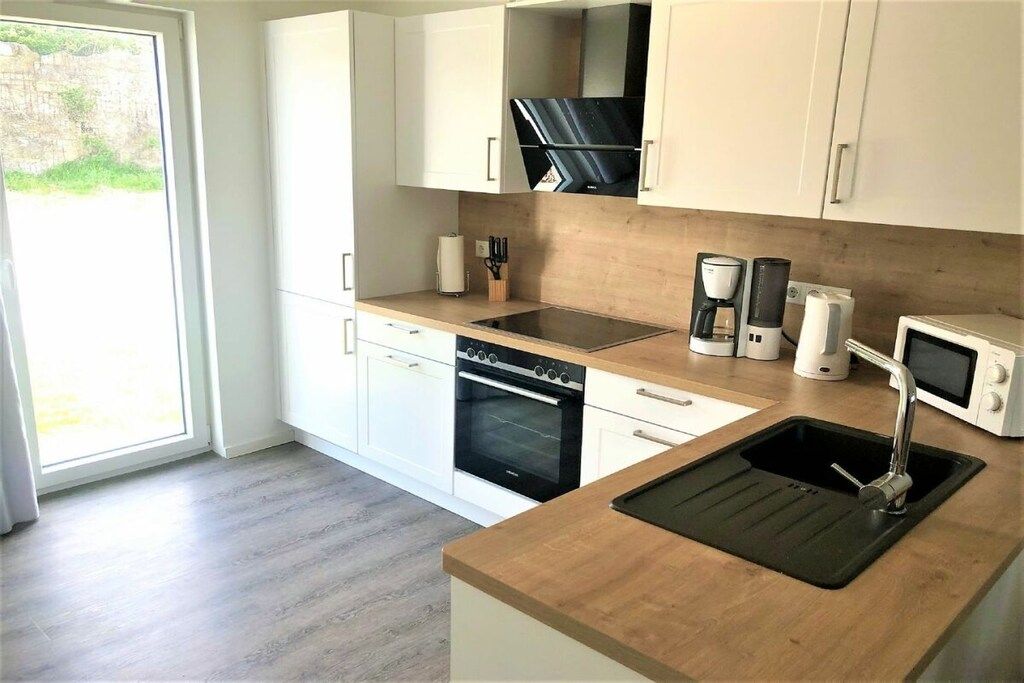 A modern kitchen with white cabinets, a built-in oven, a microwave, a coffee maker, and a sink.