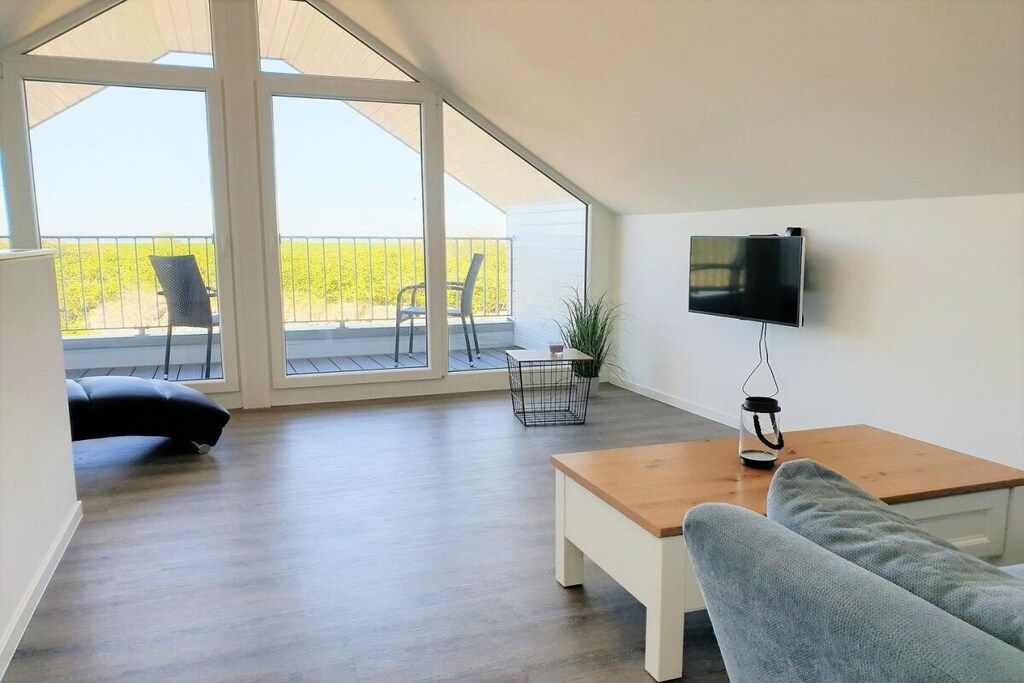 Una sala de estar moderna con un televisor de pantalla plana, una mesa de centro de madera, un sofá gris y un balcón con sillas.