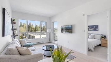 A modern living room with a sofa, a coffee table, and a view of a cityscape through large windows.