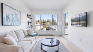 A modern living room with a sofa, a coffee table, and a large window with a view of trees and buildings.