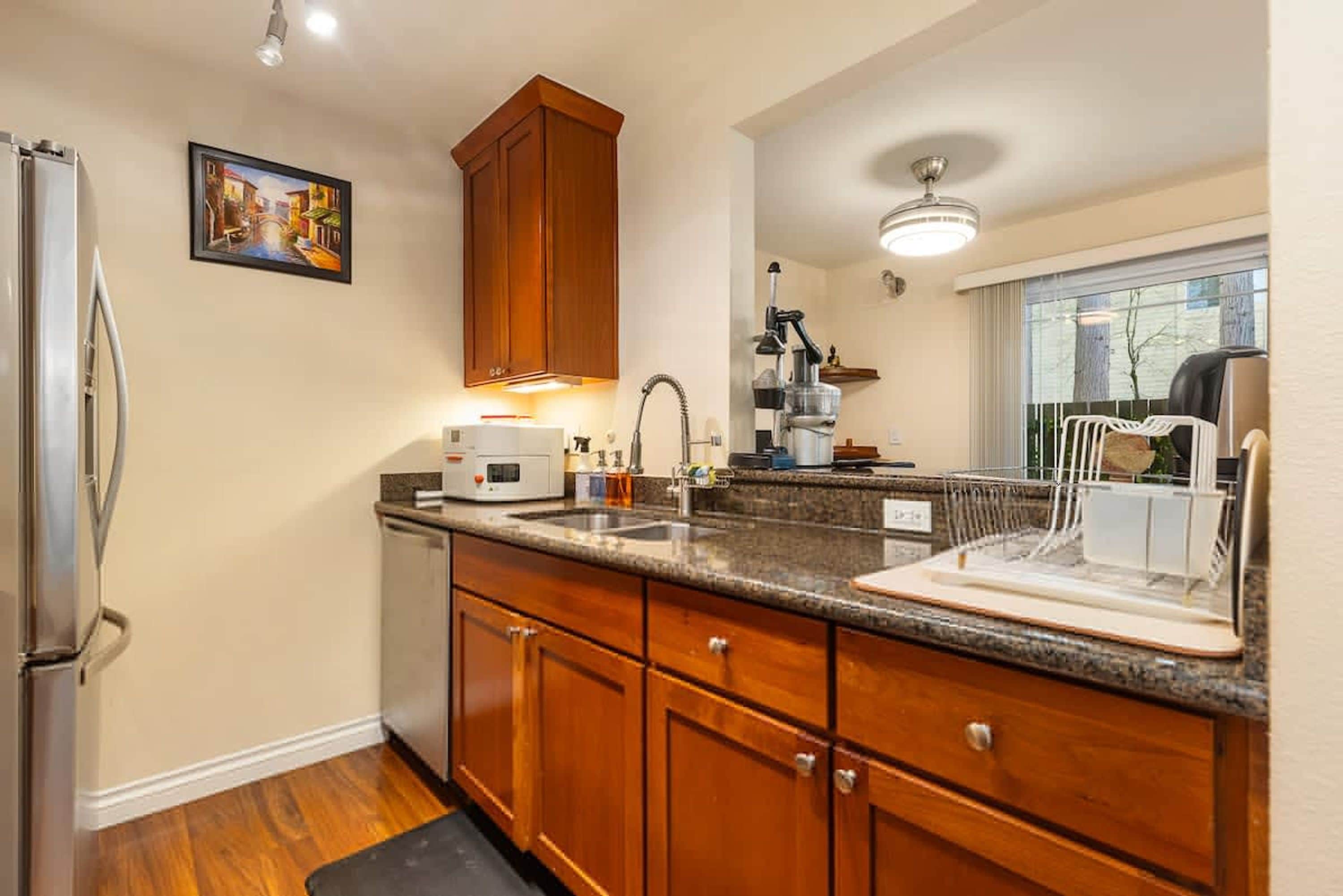 A kitchen with wooden cabinets, a stainless steel refrigerator, a microwave, and a sink.