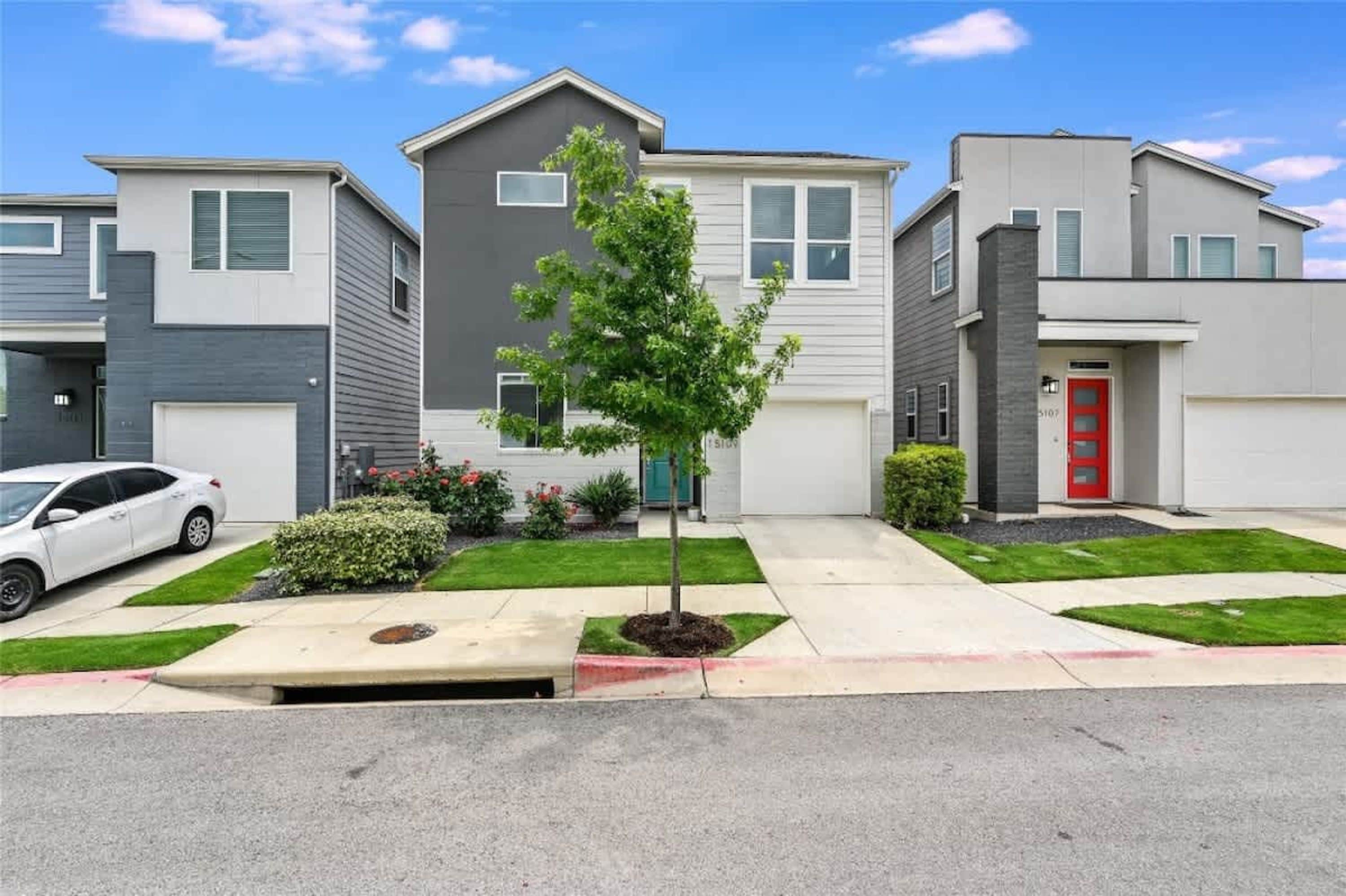 A modern residential building with a central tree, a red door, and a white car parked in front.