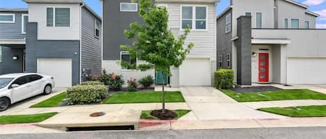 A modern residential building with a central tree, a red door, and a white car parked in front.