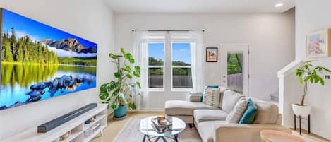 A living room with a flat-screen TV, a sofa, a coffee table, and a ceiling fan.