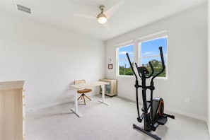 A room with a ceiling fan, a desk, an exercise bike, and a window with a view of greenery. - Spacious 2BR Flex Room Home Near Tech Campuses (Pflugerville)