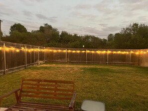 A backyard with a wooden fence, a bench, and string lights. - Spacious 2BR Flex Room Home Near Tech Campuses (Pflugerville)