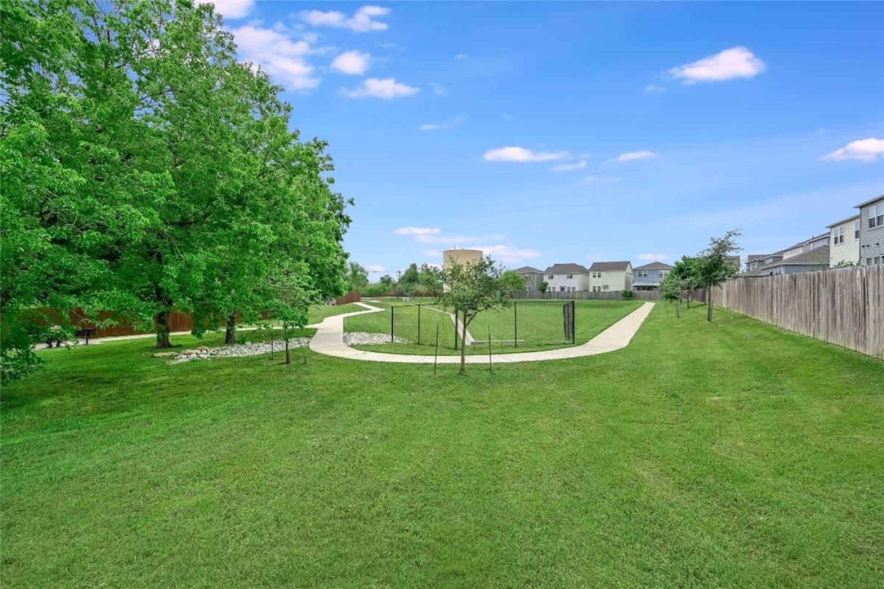 Un quartier résidentiel doté d’une pelouse bien entretenue, d’un chemin sinueux et d’une rangée de maisons délimitées par une clôture en bois.