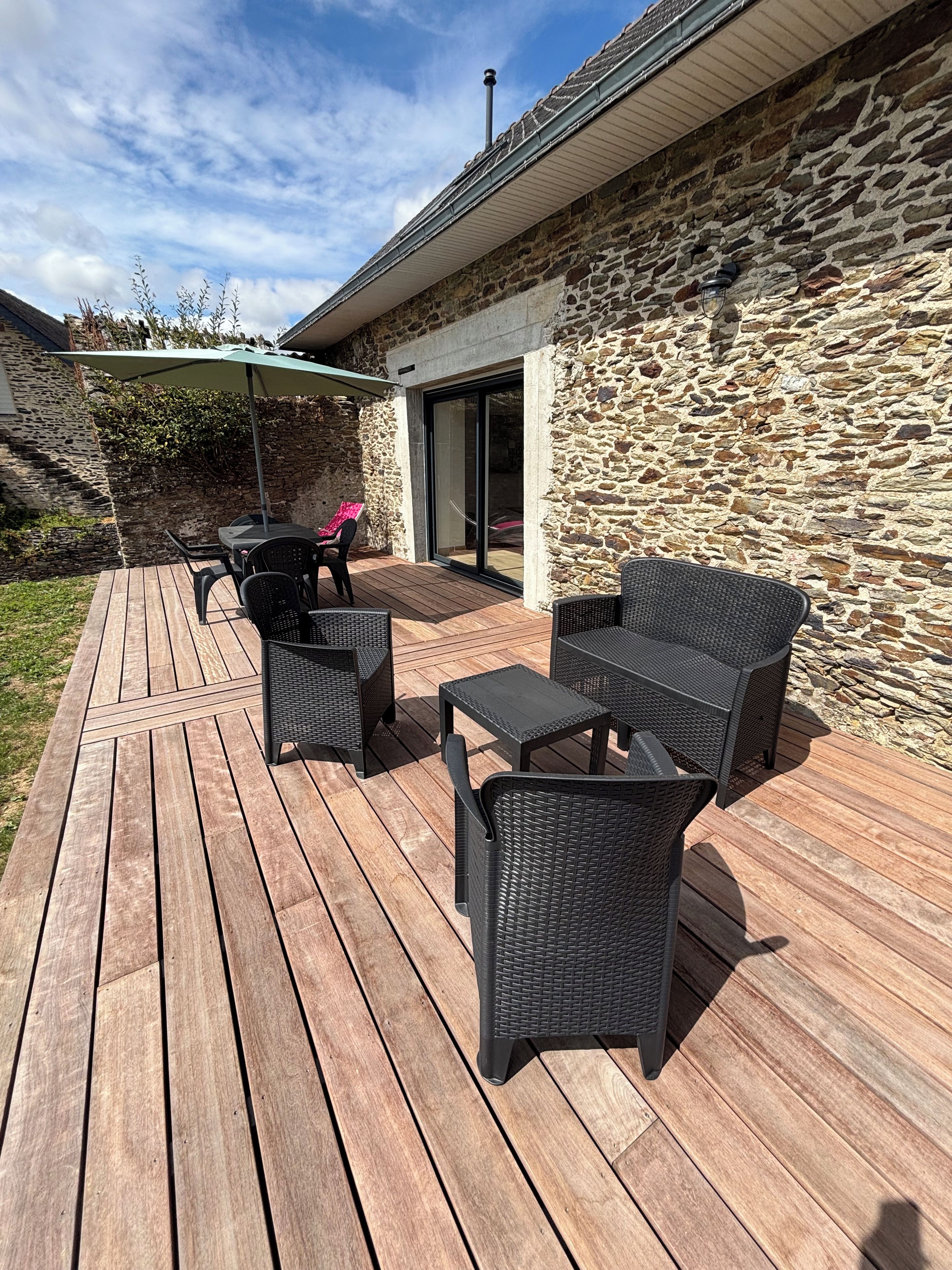 A wooden deck with outdoor furniture, a stone wall, and a covered patio area.