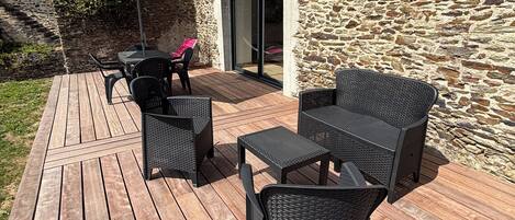 A wooden deck with outdoor furniture, a stone wall, and a covered patio area.