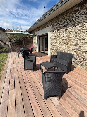 A wooden deck with outdoor furniture, a stone wall, and a covered patio area. - Fully renovated rural vacation rental (Pleyben)