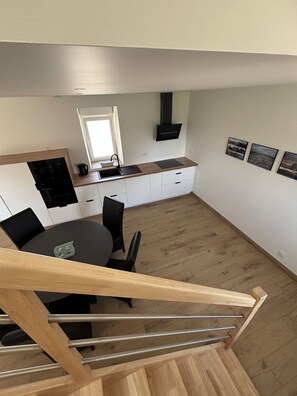 A modern kitchen with a dining area, wooden flooring, and a staircase leading to an upper level. - Fully renovated rural vacation rental (Pleyben)
