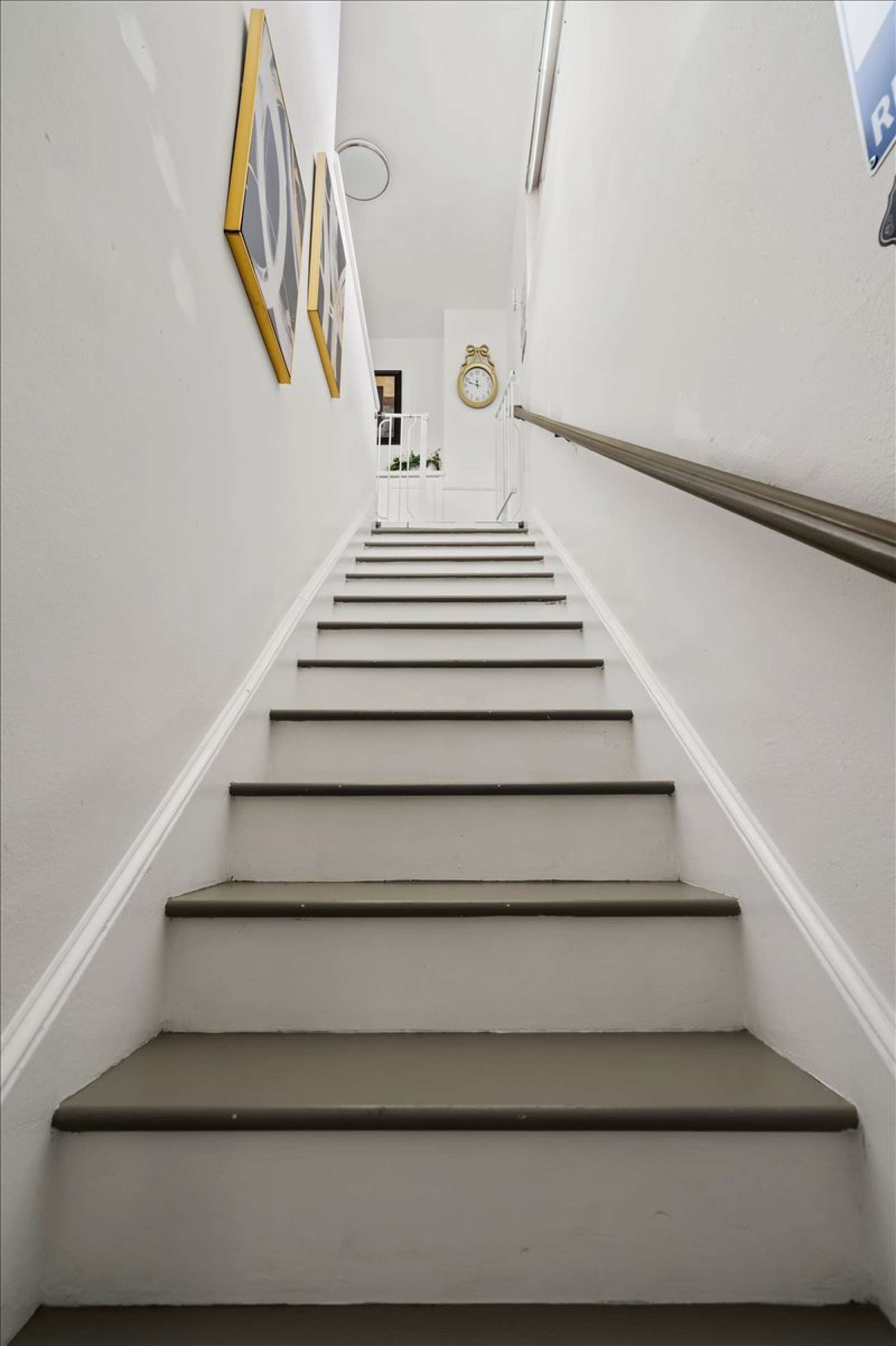 A staircase with a handrail, leading to a door with a clock on the wall.