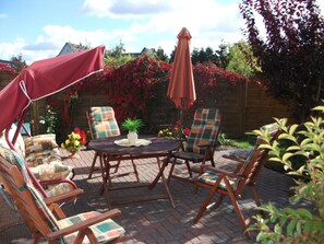 Eine Terrasse im Freien mit einem runden Tisch und vier Stühlen, umgeben von einem Holzzaun und blühenden Pflanzen.