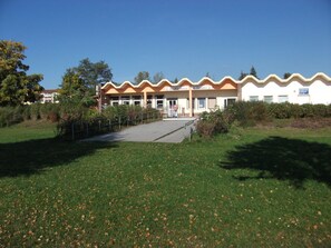 Ein Gebäude mit wellenförmiger Dachlinie, einem gepflasterten Eingangsbereich und einer Rasenfläche davor.