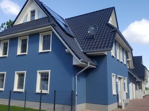 Un edificio residencial de dos pisos con fachada azul oscuro, detalles blancos y techo inclinado.