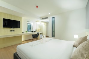A hotel room with a bed, a desk, a flat-screen TV mounted on the wall, a window, and a door. - Canvas Hotel Pattaya (Pattaya)