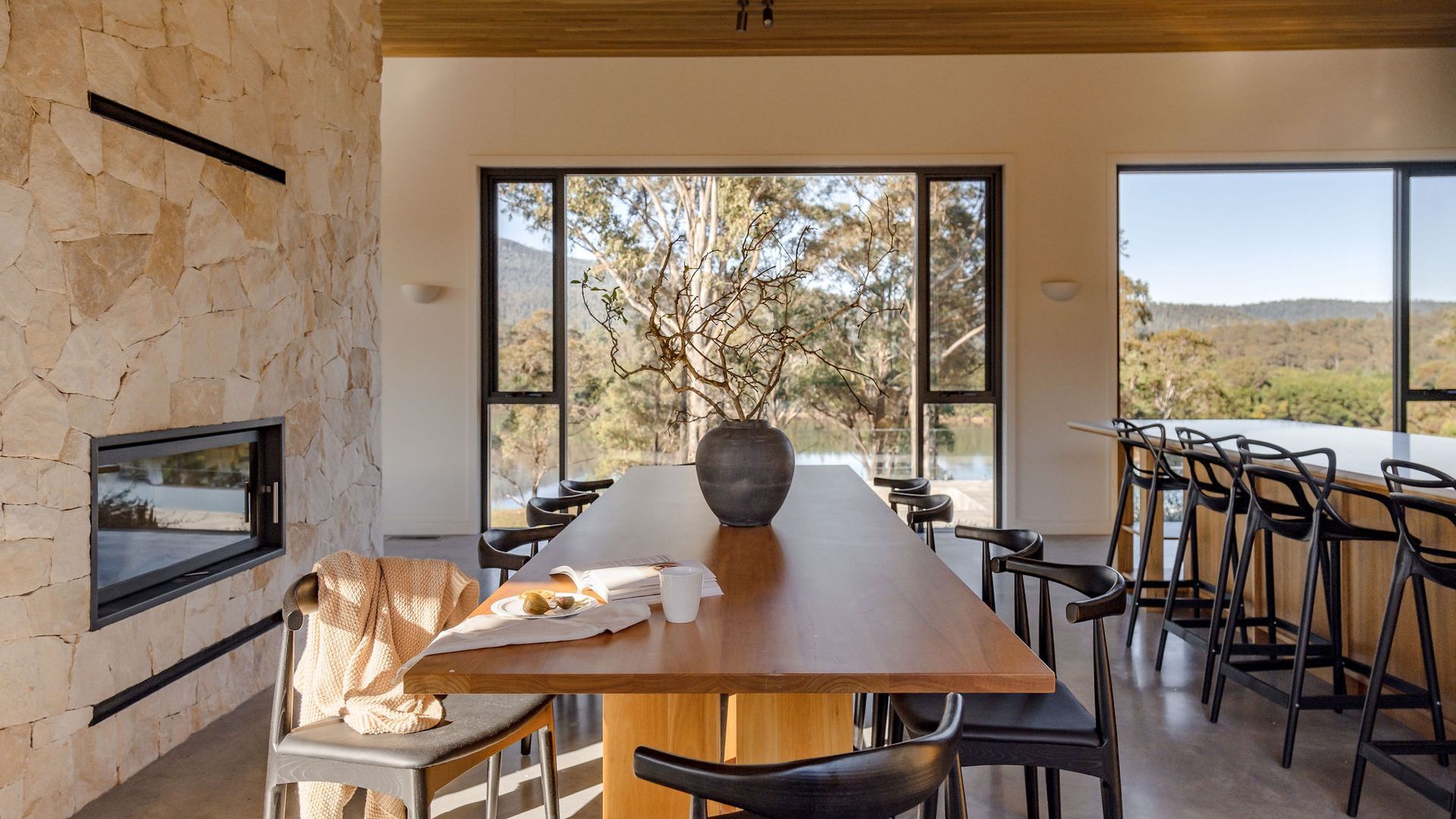 A dining area with a stone wall, a wooden table, and a view of trees and hills.