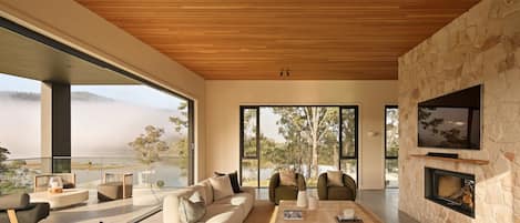 Una sala de estar moderna con chimenea de piedra, ventanas amplias y vistas a un paisaje natural.