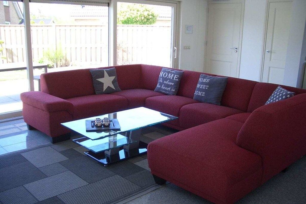 A red sectional sofa with a glass coffee table in a room with a sliding glass door leading to a backyard.