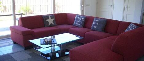 A red sectional sofa with a glass coffee table in a room with a sliding glass door leading to a backyard.