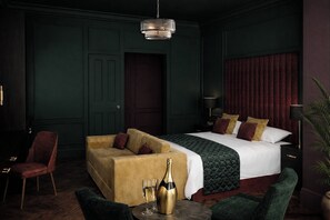 A room with a bed, a sofa, a chair, a table with glasses and a bottle, and a hanging light fixture.