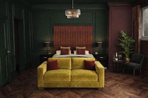 A room with a large bed, a sofa, a wooden floor, a wall-mounted light fixture, and a potted plant. - Sweeney Inverness (Inverness)