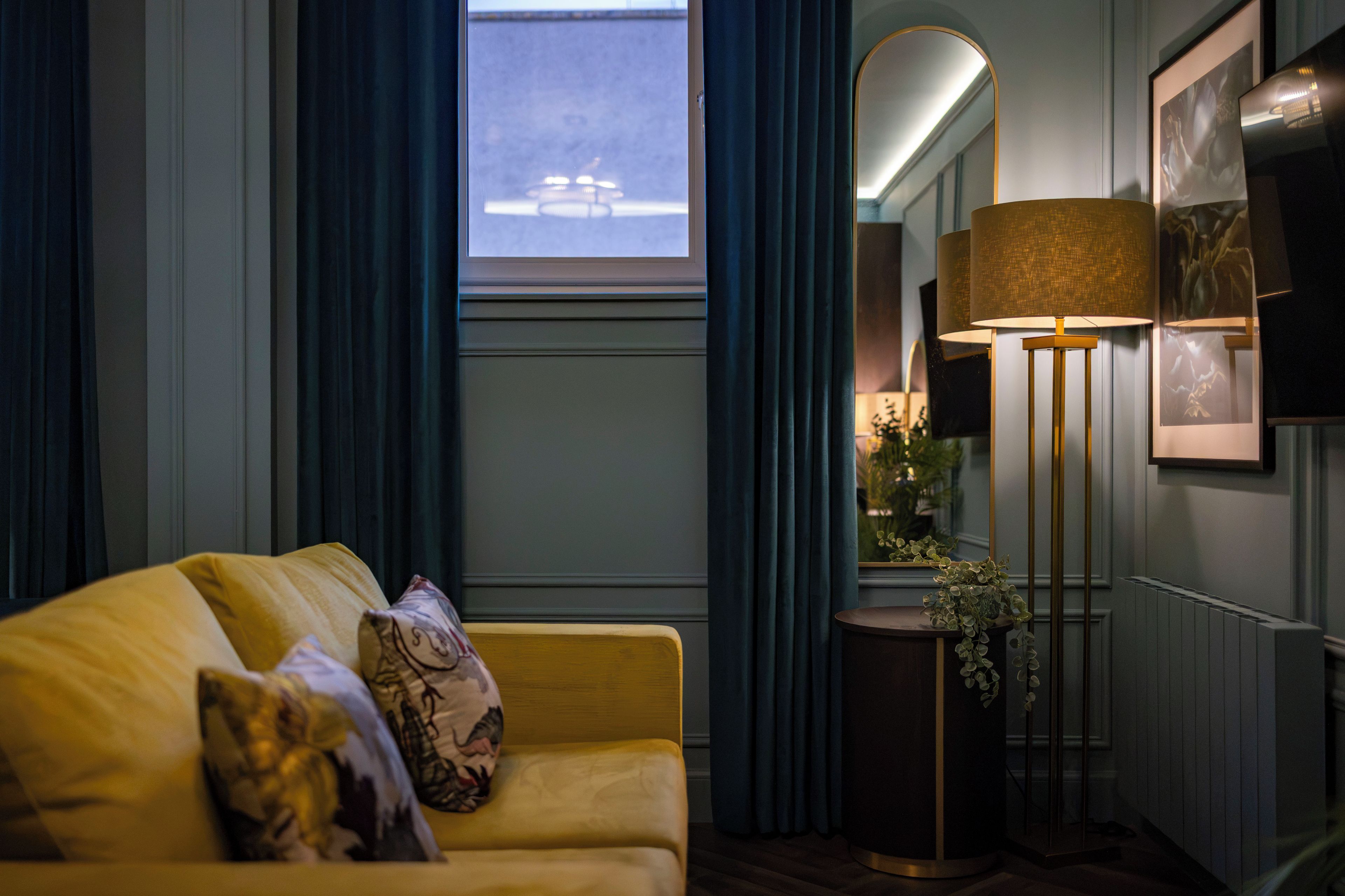 A room with a sofa, a floor lamp, a mirror, and a window.