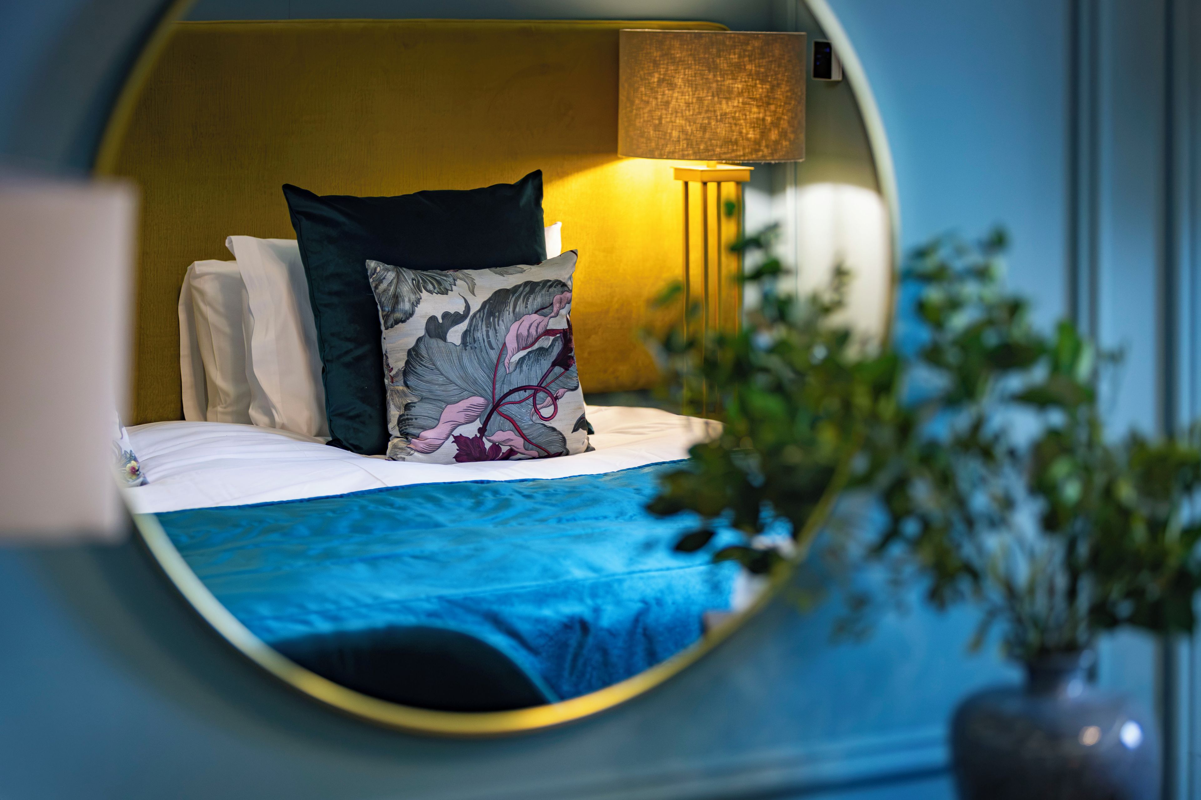 A circular view of a hotel room with a bed, pillows, a lamp, and a plant.