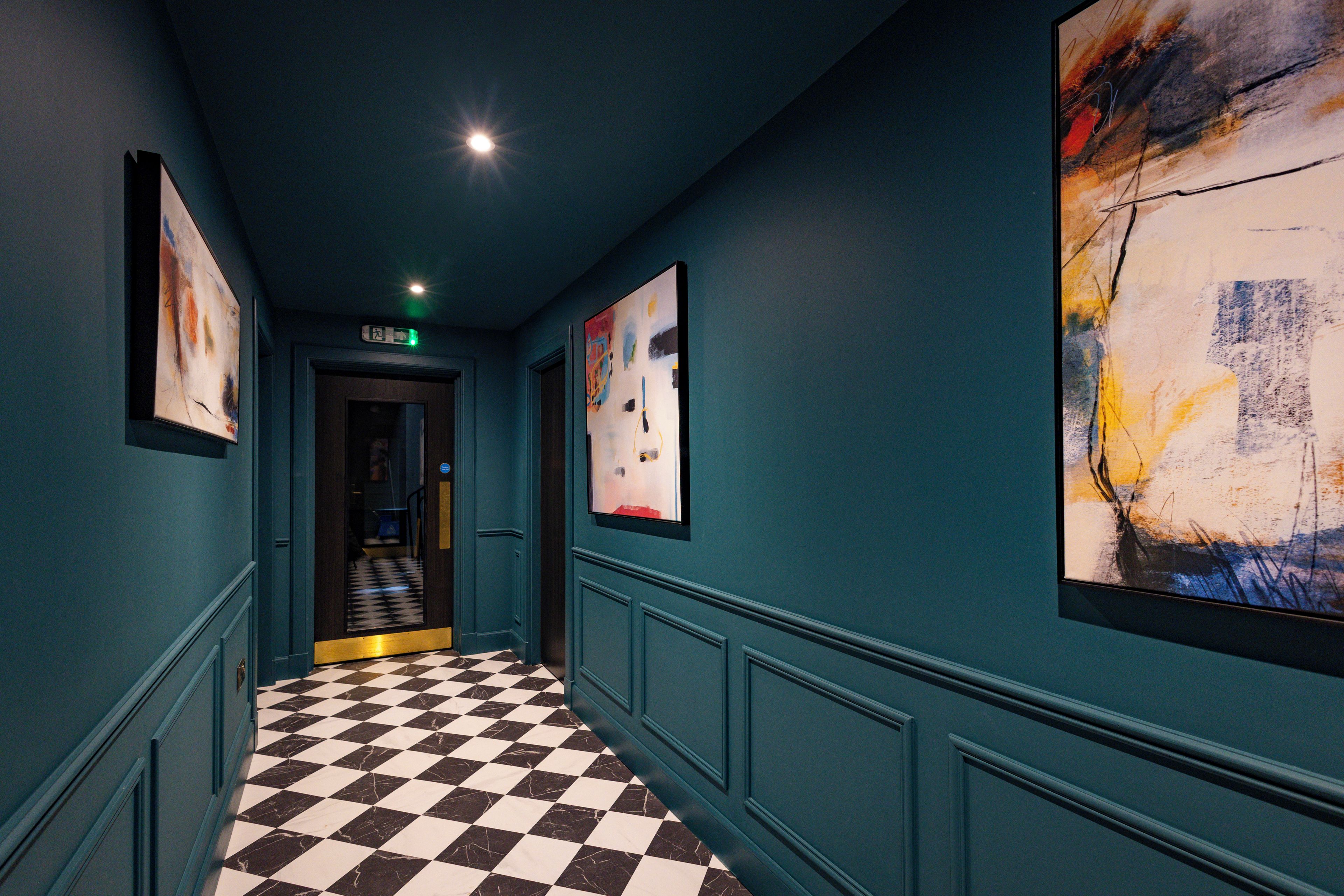 A hallway with a checkered floor, teal walls, and framed artwork.
